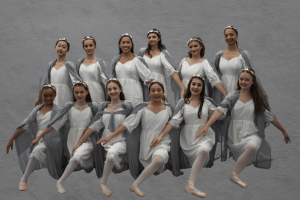 12 girls age 10-18 pose against a gray backdrop, wearing white dresses, ballet shoes, and gray robes. 
