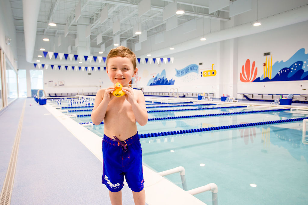 child holding rubber duck in front of big blue swim school pool