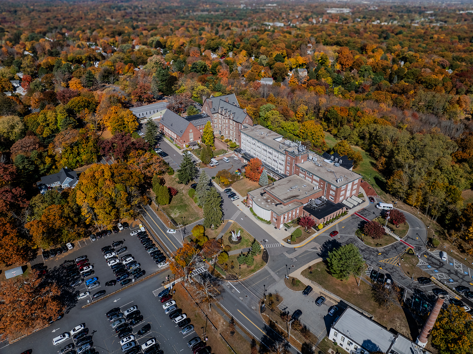 An aerial view of a building and a parking lot, with lots of colors on the leaves of the trees